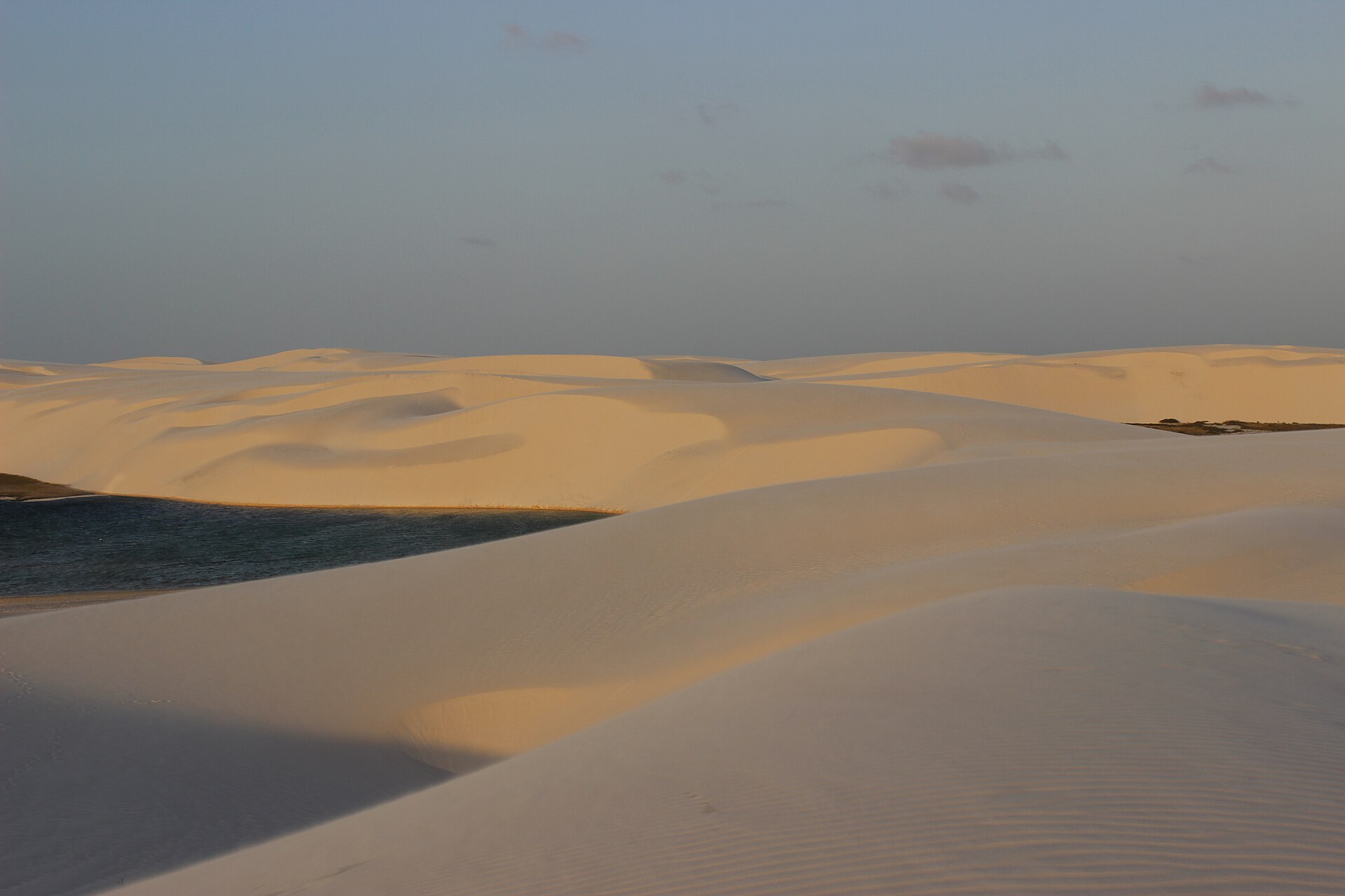 Dunas claras e lagoa entre as cristas no Parque Nacional dos Lençóis Maranhenses.