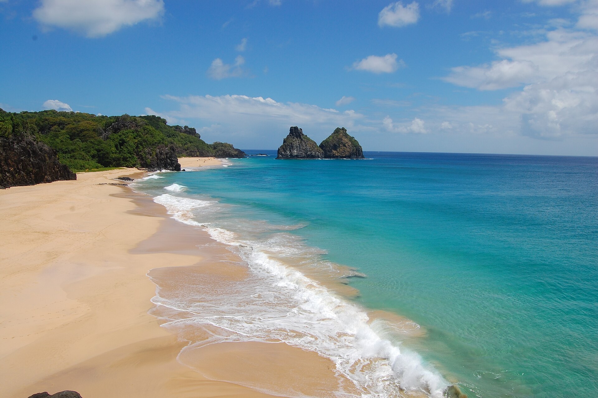 Praia em meia-lua, mar em degradê e os Morros Dois Irmãos em Fernando de Noronha.